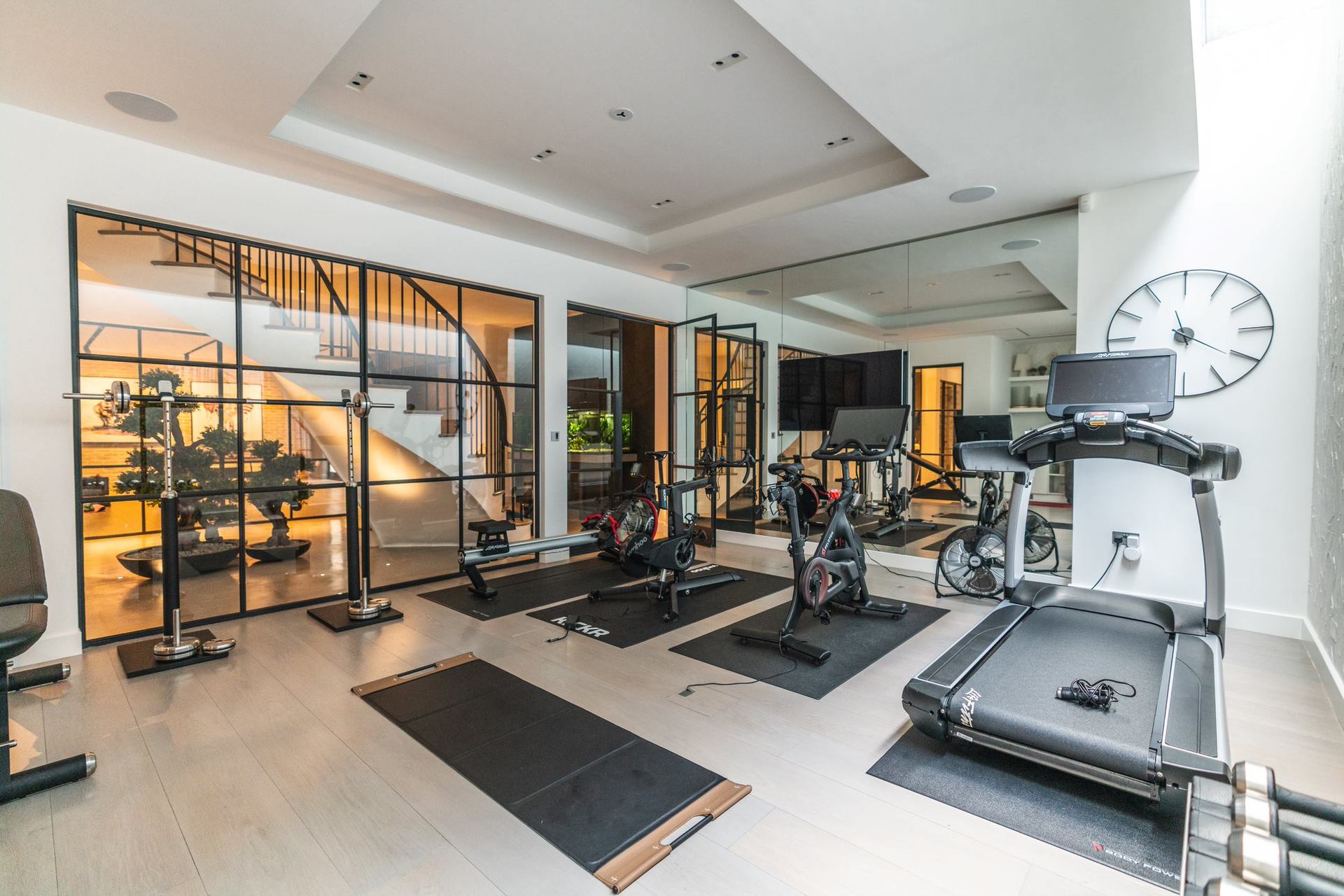 Modern gym with luxury curved staircase shown through glass in background